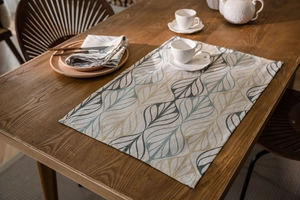 Detailed close-up of a leaf-patterned linen placemat on a wooden dining table surface