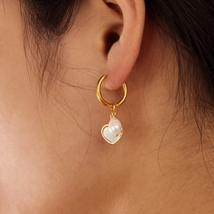 Elegant gold heart earrings with white pearl detail shown worn on ear for minimalist style