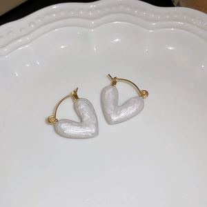 Macro shot of pearl-white heart earrings with golden metal clasps on a ceramic tray