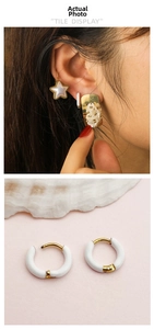 Detail of white enamel hoop earrings with gold trim worn in a stylish stacked earring set
