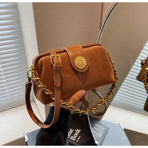 Detail of vintage brown suede crossbody bag with gold metal emblem and chain strap