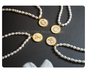Detailed view of baroque pearl necklaces with golden seashell initial letter pendants