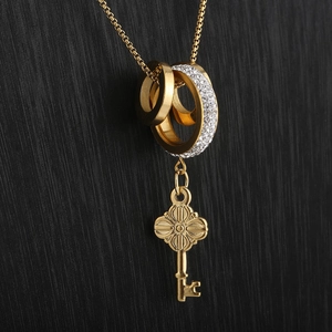 Close-up of interlocking gold rings with pavé crystals and a key pendant necklace