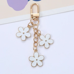 Detail of gold keychain featuring white enamel flower charms and polished metal finish