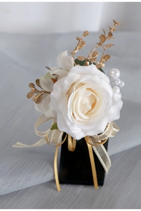 Dettaglio di fiore all'occhiello rosa bianca con foglie dorate, perle e fiocco
