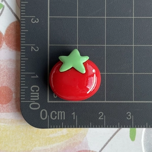 Macro shot of a red resin tomato charm showing 1.5cm width measurement on a ruler