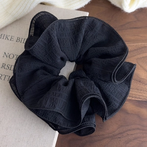 Close-up of a large black oversized scrunchie with layered ruffles and textured chiffon fabric