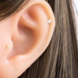 Titanium G23 piercing studs with 3mm zircon in gold finish shown on ear lobe and cartilage