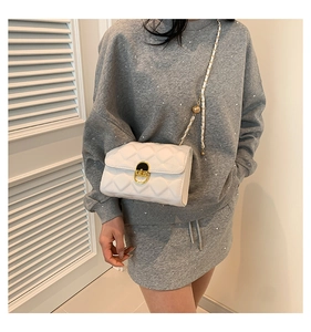 White quilted crossbody bag with golden clasp and chain strap shown on model's shoulder