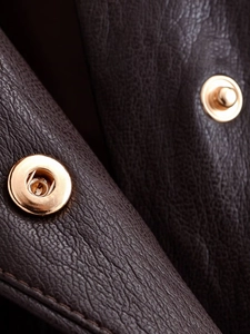 Close-up of dark brown pebbled faux leather texture with a polished gold metallic button