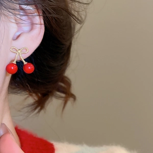 Close-up of a model wearing cherry bow earrings with red beads and golden texture