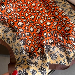 Detail of silk-like scarf featuring red leopard print and beige floral patterns with border