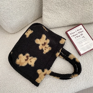 Detailed flat lay of black fuzzy bear tote bag next to a book on white fleece background