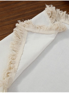 Close-up of white woven cotton linen table runner with elegant fringe edges on wood