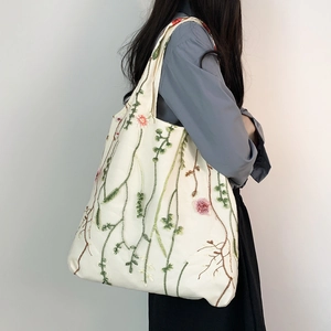 Dettaglio del ricamo floreale su una borsa tote in tela crema indossata da una modella