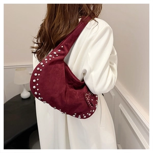 Détail de rivets argentés sur sac hobo en daim bordeaux porté par un mannequin
