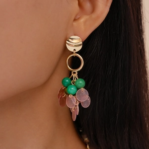 Close-up of vintage geometric gold earrings with green beads and pink pendant on a model