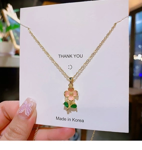 Close-up of a delicate golden necklace featuring a pink flower pendant and green gemstone leaves