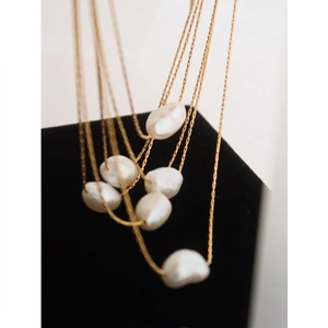 Irregular baroque pearl necklace in layered gold titanium steel on a black stand