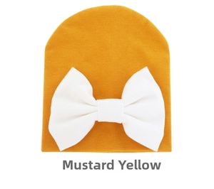 Detail of a ginger yellow knit baby beanie featuring a large white decorative bow