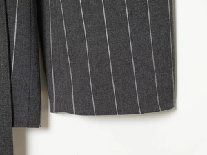Detail of dark grey pinstripe woven trousers showing the fabric texture and hemline