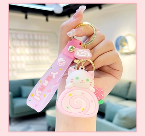 Pink cat cake roll keychain with Yummy silicone strap held against a blurred background