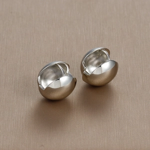 Close-up of minimalist silver spherical huggie earrings with polished mirror finish