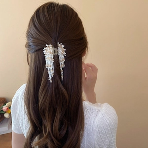 Detail of faux pearl tassel hair claw clip worn on deep brown curly hair style