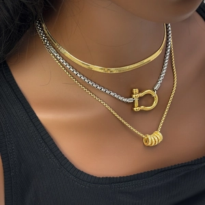 Close-up of layered 18K gold and silver necklaces with U-clasp and ring charms