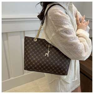 Detail view of brown tote bag with geometric floral print and gold deer charm on shoulder