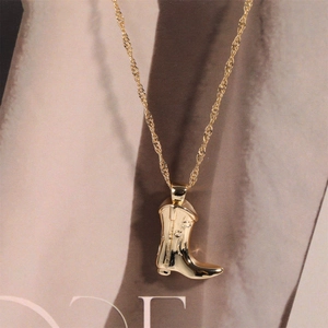 Detail of a gold cowboy boot pendant on a twisted rope chain over a fashion magazine