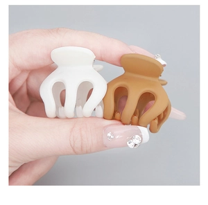 Close-up of matte pumpkin-shaped claw clips in beige and caramel on hand