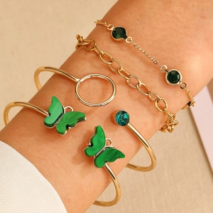 Golden bracelet set with emerald green gems and butterfly charm on a female wrist