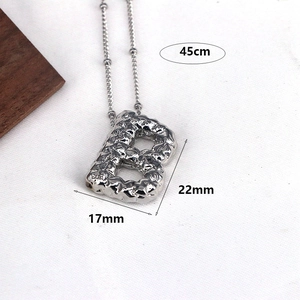 Macro detail of silver letter B pendant with lava texture and dimensions 22x17mm