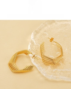 Macro shot of gold U-shaped geometric earrings with multi-layered wire design on beige velvet