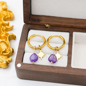 Macro detail of star charms and purple gemstone pendants on gold-plated hoop earrings