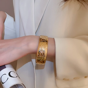 Detailed close-up of wide gold bangle featuring intricate scrollwork floral engraving