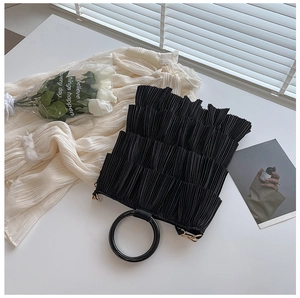 Detail of black pleated tote bag with round handle and layered texture on white surface