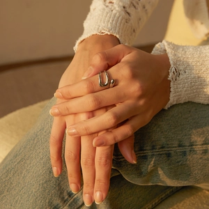 Detail of silver asymmetric double-layered open ring on hand in warm lighting