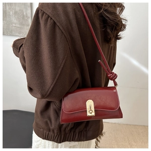 Detail of dark red faux leather shoulder bag with gold clasp and elegant knot strap