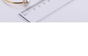 Macro shot of minimalist gold bangle with large pearl detail and size measurement scale