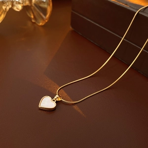 Gros plan d'un collier coeur doré avec incrustation en nacre blanche sur fine chaîne serpent