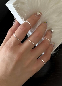 Detailed view of five textured silver stackable rings on hand with a textured foil finish