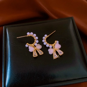 Detail of gold C-shaped earrings with pearls, pink bows and sparkling zircon ribbons