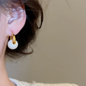 Close-up of elegant gold-plated U-shaped earrings with textured pearl beads on a model