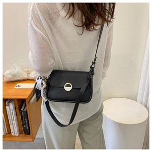 Detail of black leather crossbody bag with metal ring buckle and polka dot scarf accessory