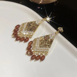 Close-up of diamond-studded rhombic tassel earrings with brown beads on white ceramic