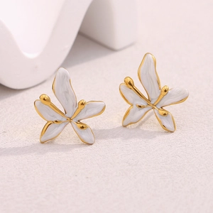 Vue macro de boucles d'oreilles fleurs dorées avec émail blanc et détails métalliques fins