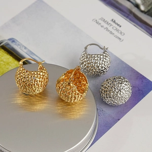 Detailed close-up of gold and silver hollow woven basket-style hoop earrings on a metal tray