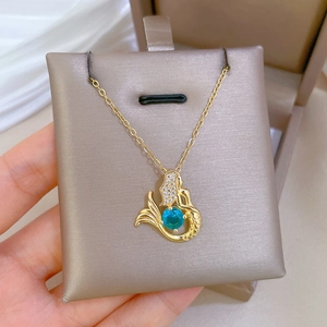 Close-up of golden mermaid necklace with blue sapphire gemstone on silk cushion
